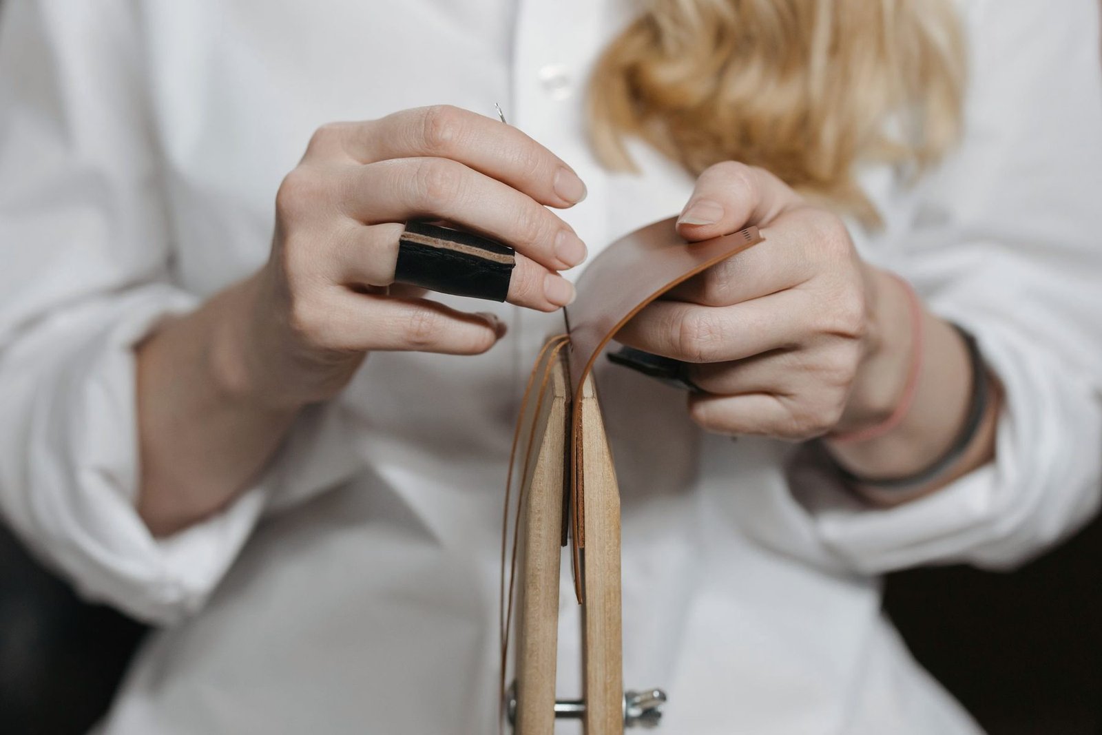 Hands stitching a leather strap by hand.